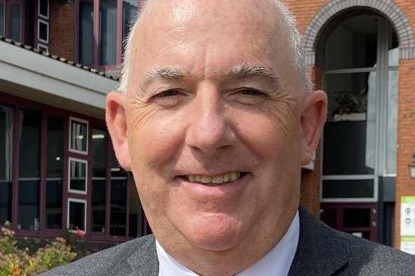 Kim Bromley-Derry, a middle-aged man with short grey hair, wearing a grey suit and white shirt. He is smiling at the camera