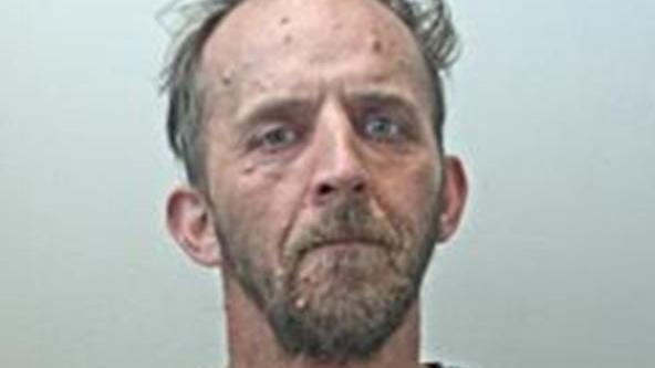 Police custody image of Aaron Cane with brown beard and receding brown hair wearing a grey t-shirt.