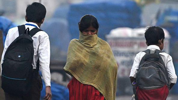 A woman covers her face as she walks past school boys on a cold smoggy morning in the old quarters of New Delhi in November 2024