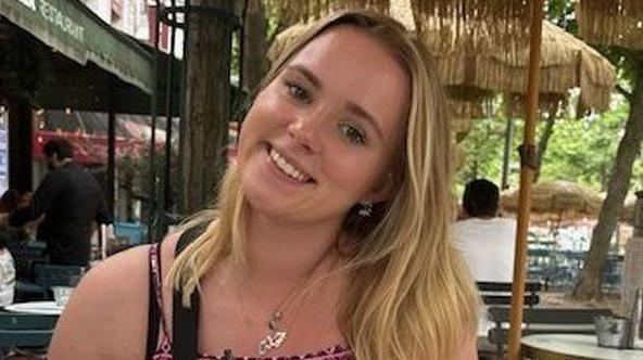 Jamilla Blake, who is wearing a patterned top with straps and has long blonde hair, smiles as she sits at a restaurant table.