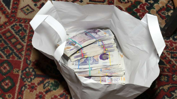 A white bag containing bundles of £20 notes.