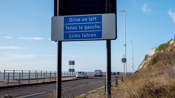 A blue sign reminding drivers to drive on the left side of the road.