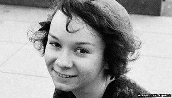 Black and white picture of a woman wearing a light coloured beret and smiling up at the camera with paving stones behind her