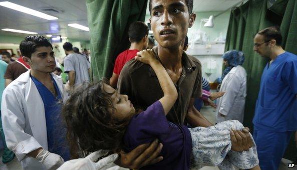 A Palestinian man carries a child, apparently wounded in an Israeli strike on a compound housing a UN school in Beit Hanoun, in the northern Gaza, into the emergency room of the Kamal Adwan hospital in Beit Lahiya, Thursday 24 July 2014