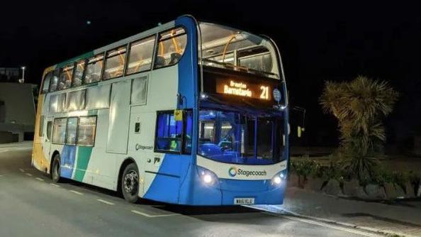 A blue, white and green bus travelling along a road at night