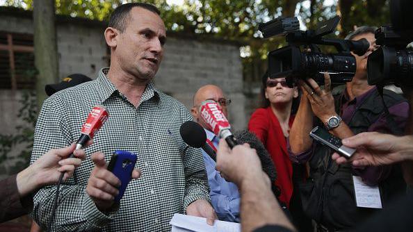 Cuban activist Jose Daniel Ferrer speaking to journalists in 2015. Several journalists are standing around him with mics as he speaks. One is holding a camera. 