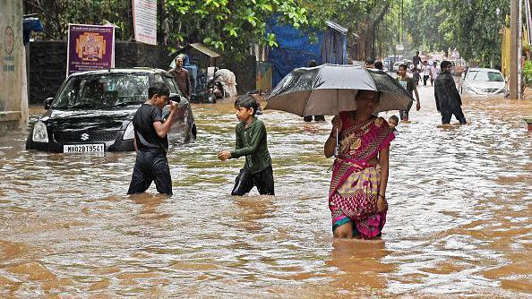 A woman holding an umbrella walks on a street flooded with water due to heavy rain in Mumbai.