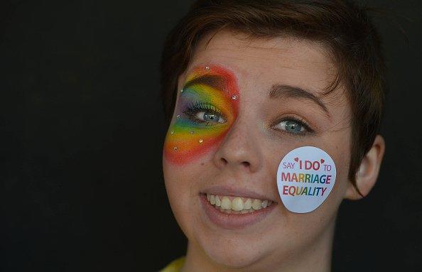 Woman with equality sticker on her cheek and rainbow painted on her eye