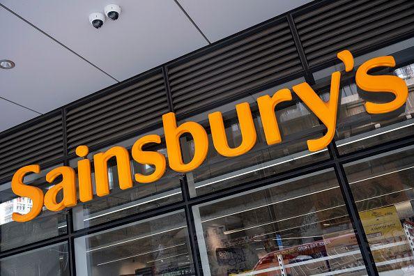 A large orange Sainbury's sign can be seen on the front of a supermarket above the shop's glass windows.