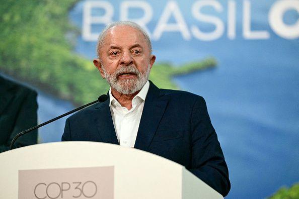 President Lula in white shirt and dark blue suit jacket with a backdrop of a poster of the Amazon and the COP30 logo