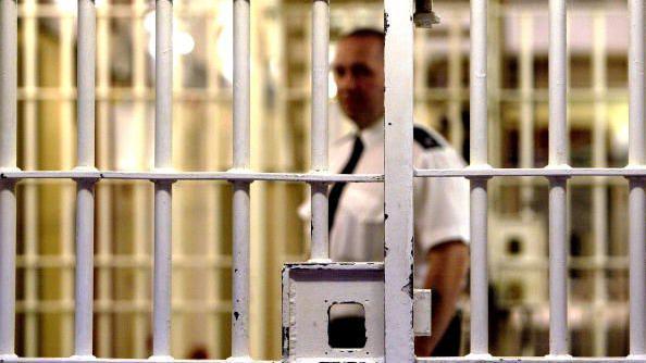 A prison officer stands behind bars in a jail