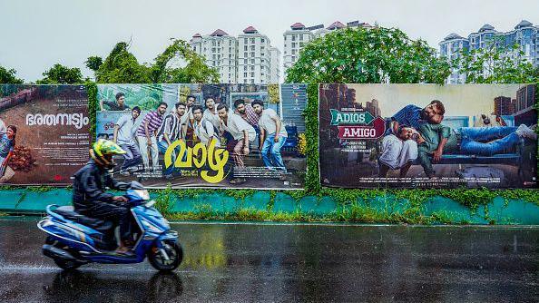 A man rides past posters of regional movies from India's Kerala-based Mollywood film industry, displayed along a street amid protests against alleged sexual allegations within the industry, in Kochi on August 30, 2024. 