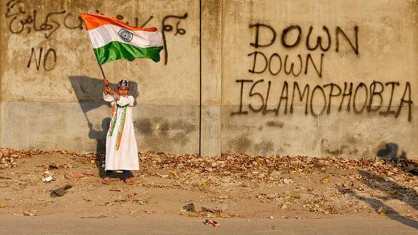 A young boy stand holding the national flag next to a wall that says 'Down down Islamophobia'