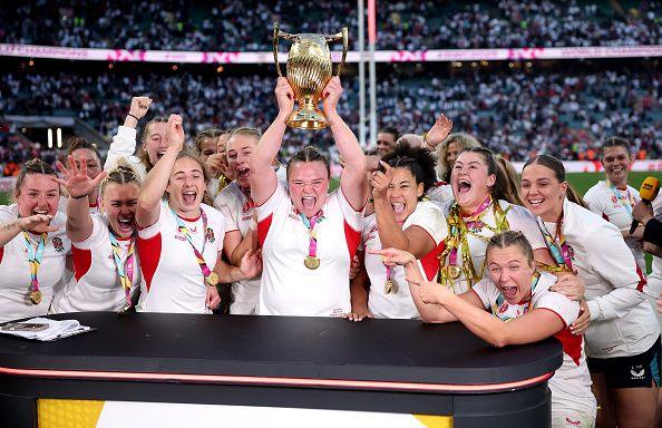 Sarah Bern lifts the Women's World Cup Trophy whilst (L-R) Amy Cokayne, Rosie Galligan, Emma Sing, Abby Dow, Jess Breach, Alex Matthews, Morwenna Talling, Lark Atkin-Davies, Tatyana Heard, Maud Muir, Zoe Aldcroft, Maud Muir and Lilli Ives Campion of England celebrate with their winners medals.
