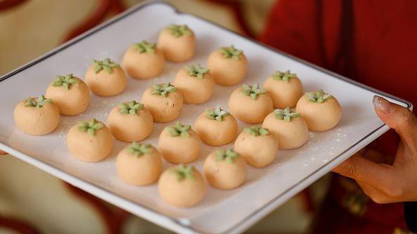 Round rice balls with green leaf decorations, being served on a white porcelain square dish