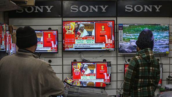 Men watch the live telecast of Finance Minister Nirmala Sitharaman's budget speech on television screens inside a shop in Srinagar