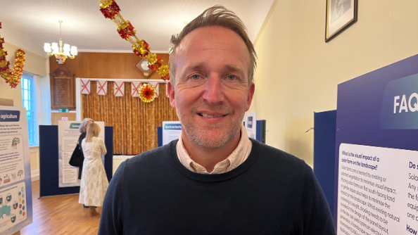 Steve Tanner pictured in a community hall wearing a navy blue jumper with a white shirt beneath it. He has mousy brown hair that has been swept to one side. 