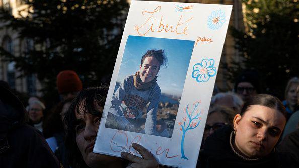 A person holds a photograph of Olivier Grondeau, showing him smiling, at a gathering in support of those arrested in Iran. 