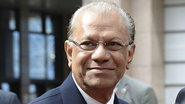 Navin Ramgoolam, wearing glasses and a suit, smiles past the camera.