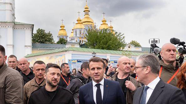 UK Prime Minister Sir Keir Starmer and French President Emmanuel Macron and Volodymyr Zelensky are surrounded by media and army personnel in front of Kyiv's golden domed churches
