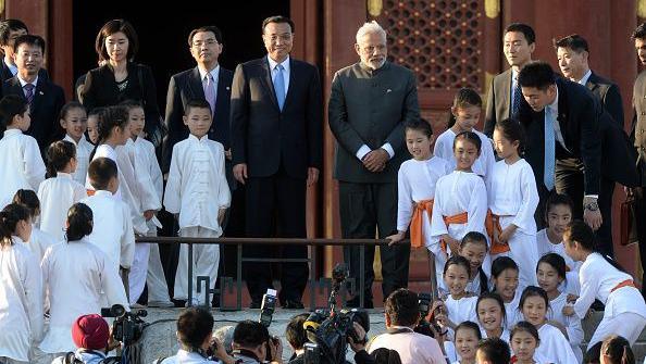 Indian Prime Minister Narendra Modi in a grey suit (standing centre right) with Chinese Premier Li Keqiang (center left) in a black suit, surrounded by child performers of the Taiji and Yoga event, at Temple of Heaven park in Beijing in May 2015. A gaggle of photographers take their photos.