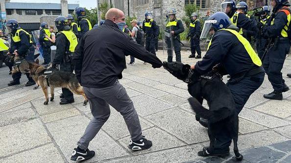 A police dog bites a man's sleeve during disorder in Plymouth