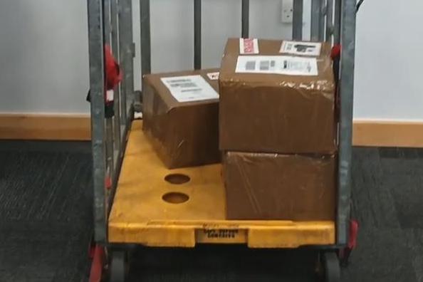 A trolley is shown in a carpeted room with three brown cardboard boxes, labelled. One of them contains the stolen phone that sparked a huge police investigation into a phone theft gang.