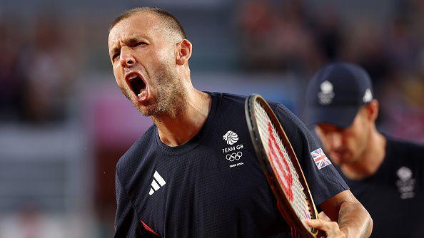 Close up of Daniel Evans as he celebrates, a blurred Andy Murray is in the background