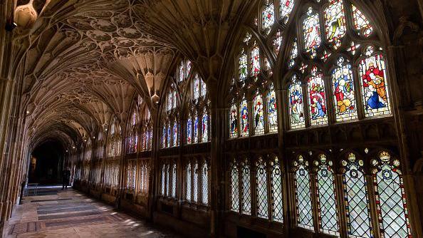 The cloisters at Gloucester Cathedral, which have vaulted, Gothic vibe ceilings and colourful stained glass windows