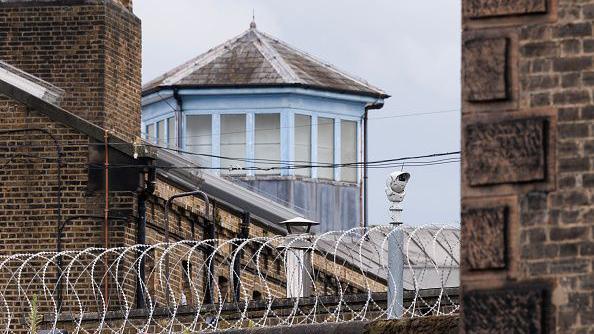 Security cameras overlook a barbed wire fence at a prison in England
