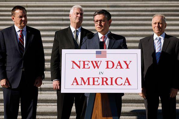 House Speaker Mike Johnson stands behind a lectern with a sign that reads "new day in America"