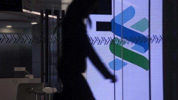 A woman walks past an illuminated Standard Chartered logo