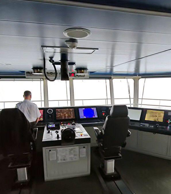 The bridge of a ferry including a member of staff who is being filmed from behind.