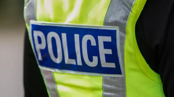 A generic image of a police officer wearing a high-vis police vest with the word 'Police' stitched into the back on a blue patch.