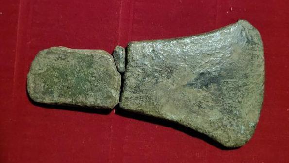 Three pieces of an old axe head, sitting in a box with a red base, after their discovery.