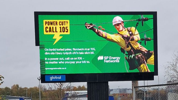 A large billboard advert for SP Energy Networks in London, showing an electricity worker working on wires, with wording in both English and Welsh saying: Os bydd toriad pwer, ffoniwch ni ar 105, dim ots i bwy rydych chi'n talu eich bil

In a power cut, call us on 105, no matter who you pay your bill to.