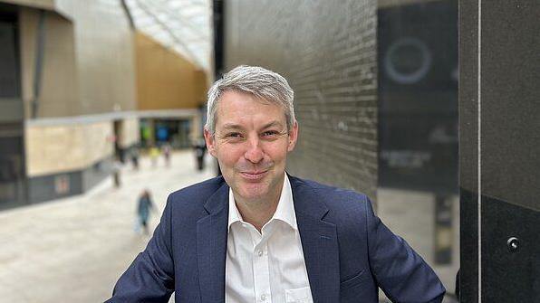 Will Forster, wearing a blue jacket and a white shirt, poses for a picture in the main foyer of the British Museum in London.