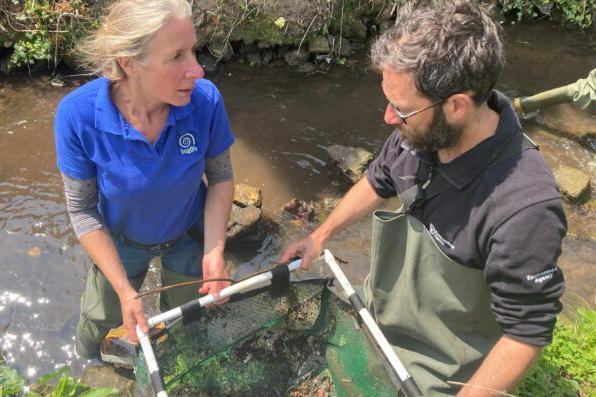 Two people working next to a lake with a net of crayfish