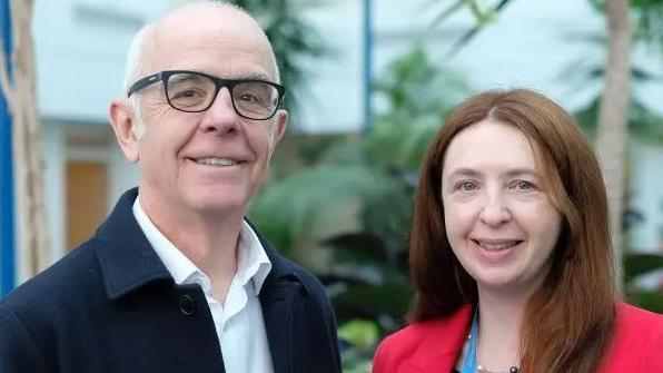 Dr Steve Evans and Michelle Le Cheminant smile while standing in front of a set of plants inside the room.