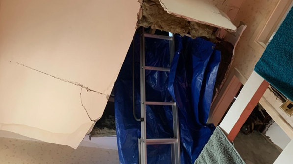 The ceiling and insulation of a house hanging down, with a ladder and blue sheeting in the gap left by the damage