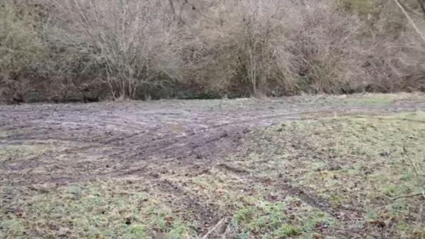 A field of short grass that appears to have been been churned up by vehicles and is now covered in muddy tyre tracks. Trees border the field at the back.