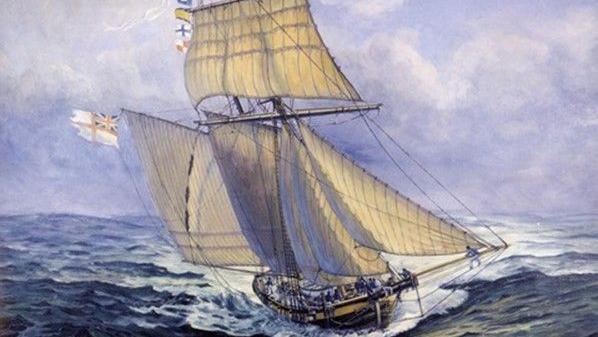 A painting of HMS Pickle, the fastest ship at Trafalgar, speeding through the water. The boat was a stopsail schooner of the Royal Navy. It is brown with cream-coloured sails and different flags on the top. The water is choppy. 