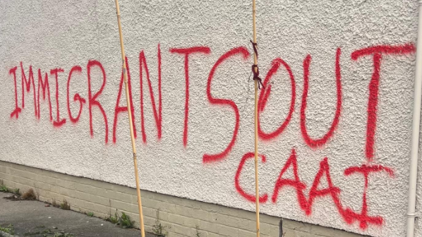 Shows a gable wall with the words "Immigrants Out CAAI" written in red paint