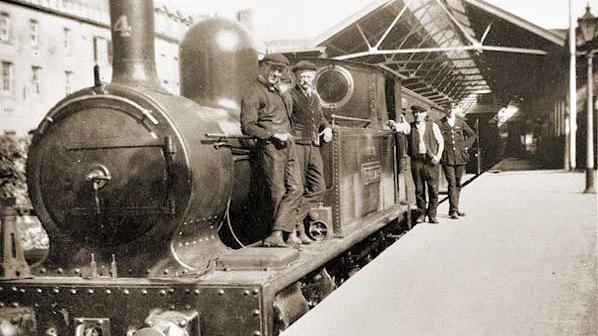 A black and white image of a steam train with four men standing next to an engine on a platform.