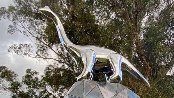 A steel dinosaur sculpture stands on top of a geometric ball in New Zealand.