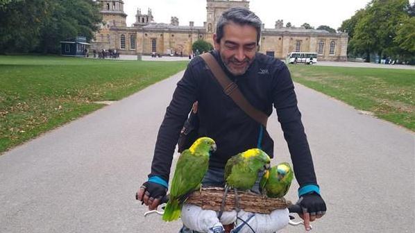 Ali Kohansal rising a bike with his parrots at Blenheim Palace