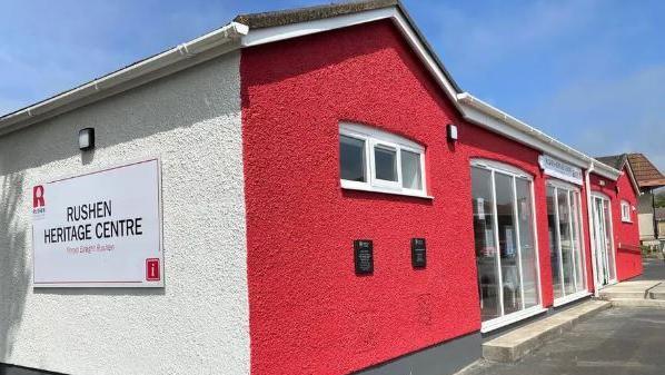 The Rushen heritage Centre, which painted white with a red front. It has large glass windows and a glass door.