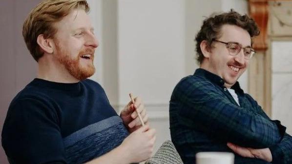 Michael (left) in a navy jumper is holding a pencil and smiling and Oisín Kearney (right) who is in a shirt and is wearing glasses.