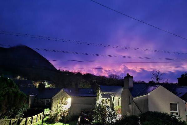 A row of houses seen below the skyline which has a blue and purple colour to it. There are power lines shooting across the sky.