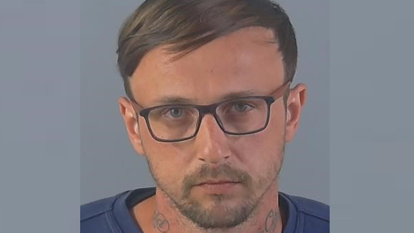 A police custody image of Kieran Bond. He has glasses, straight brown hair combed sideways, a short beard and tattoos on his neck.